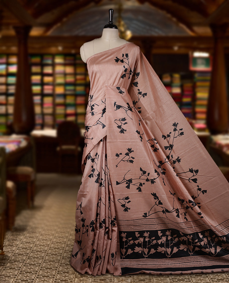 Pastel Peach colour Semi tussar silk saree adorned with black floral prints on the body and an elegant pallu & Comes with a matching blouse piece for a classy look.