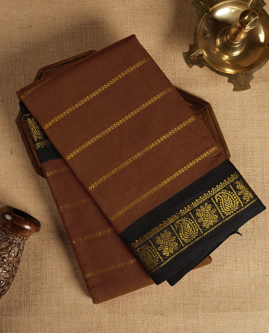 Brown colour Chettinad cotton saree accentuated with golden zari stripes all over, The contrasting black border with intricate floral motifs in golden zari  & Comes with a matching blouse piece.