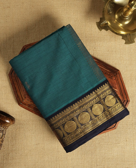 Teal blue colour Chettinad cotton saree featuring a rich contrast navy blue colour border adorned with intricate golden zari circular motifs and geometric designs & it comes with a matching blouse piece.