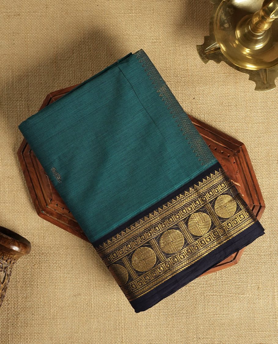 Teal blue colour Chettinad cotton saree featuring a rich contrast navy blue colour border adorned with intricate golden zari circular motifs and geometric designs & it comes with a matching blouse piece.