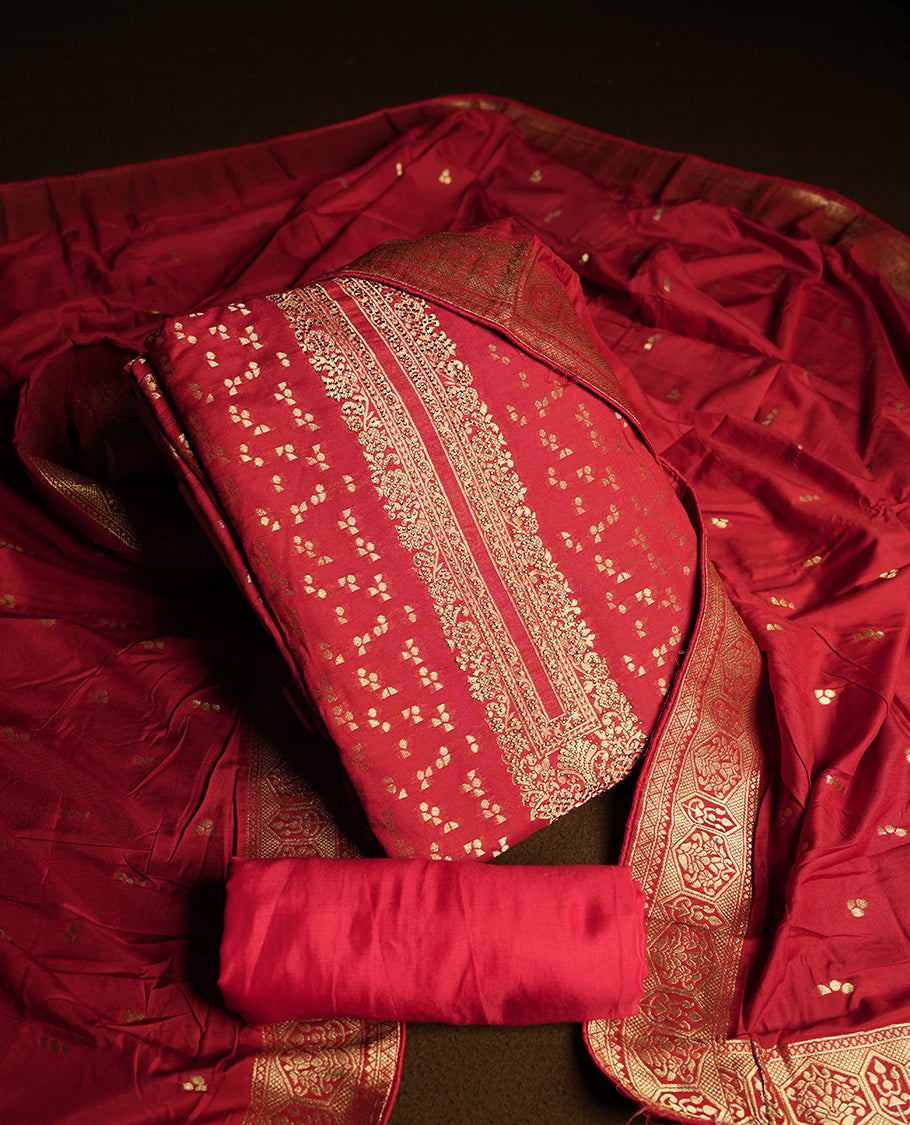 Deep maroon colour churidar material adorned with small golden stone work on the neckline, featuring intricate zari floral motifs on the body, rich zari woven border and dupatta, paired with matching plain bottom.