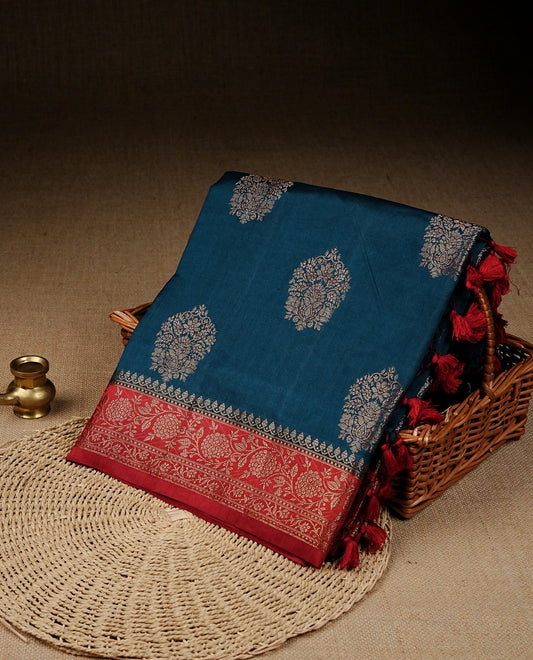 Teal blue colour banaras saree featuring gold zari motifs on body, complemented by contrast Maroon colour with gold zari border, comes with matching blouse piece.
