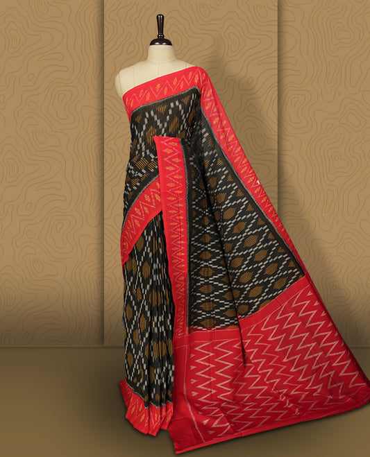 Black colour Ikkat Pochampally saree featuring a vibrant red border and pallu adorned with traditional ikat motifs in shades of beige & grey, bringing a perfect blend of heritage and modern charm.