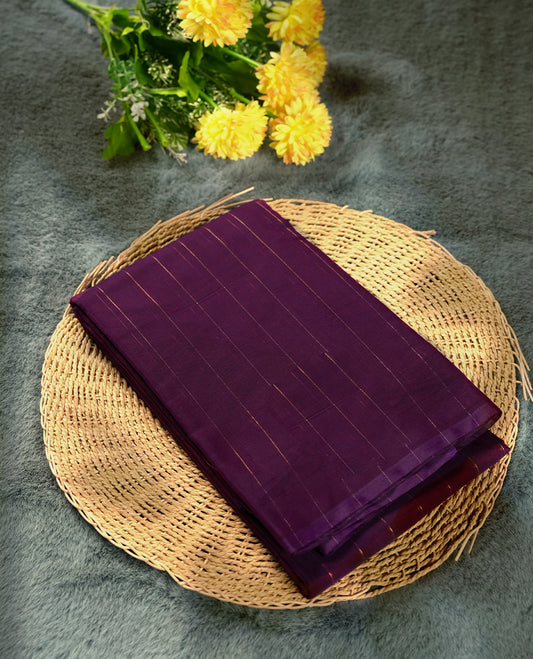 Plum purple colour silk cotton saree adorned with subtle vertical copper zari lines all over the body, crafted without a border for a minimalist charm & beige colourcontrasted border, Paired with a matching blouse for a refined, elegant look.