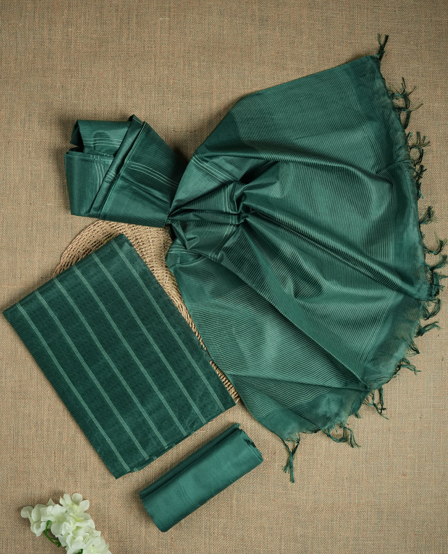Dark Turquoise green colour tussar suit material featuring a subtle self woven pattern and vertical lines on the body, paired with a lightweight matching dupatta with tassel edges and a plain bottom piece.