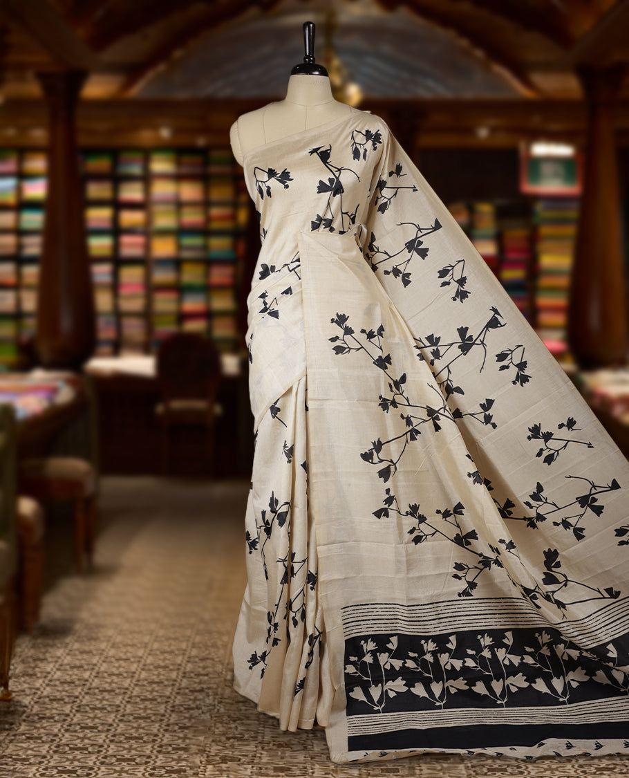 Pastel Ivory colour Semi tussar silk saree adorned with black floral prints on the body and an elegant pallu & Comes with a matching blouse piece for a classy look.