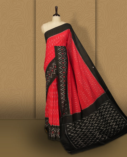 Red colour Ikkat Pochampally saree with bold zigzag motifs and contrasting black borders, The striking woven pallu enhances its elegance, making it a perfect blend of tradition and style.