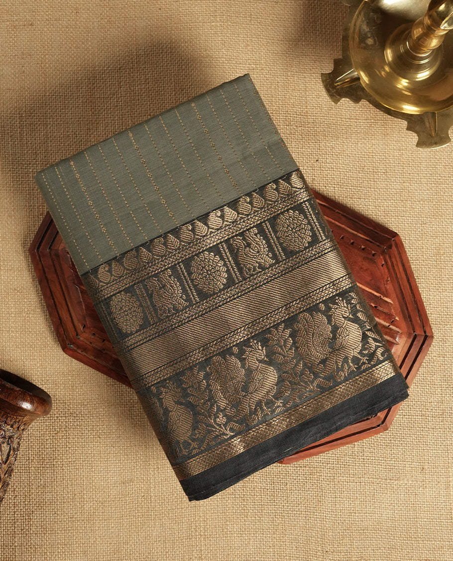 Grey colour Chettinad cotton saree adorned with subtle golden zari lines on the body, The rich ash colour border features intricate peacock and floral motifs in golden zari & Comes with a matching blouse piece.