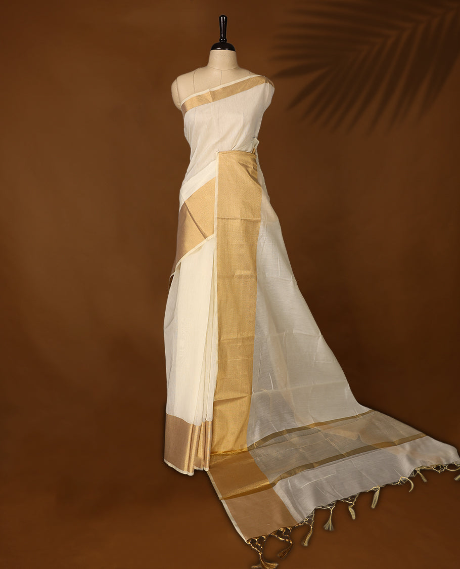 Elegant Off white colour Kerala saree with a traditional golden zari border and pallu, finished with golden tassels & A timeless ethnic piece, perfect for festivals and celebrations, paired with a matching blouse.