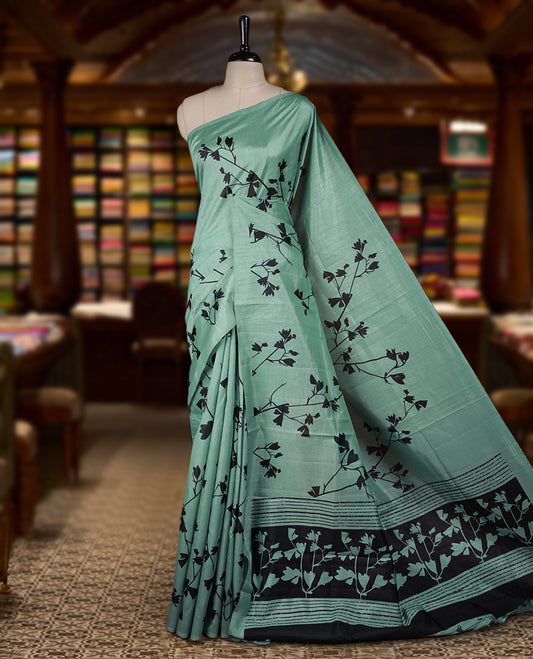 Pastel Green colour Semi tussar silk saree adorned with black floral prints on the body and an elegant pallu & Comes with a matching blouse piece for a classy look.