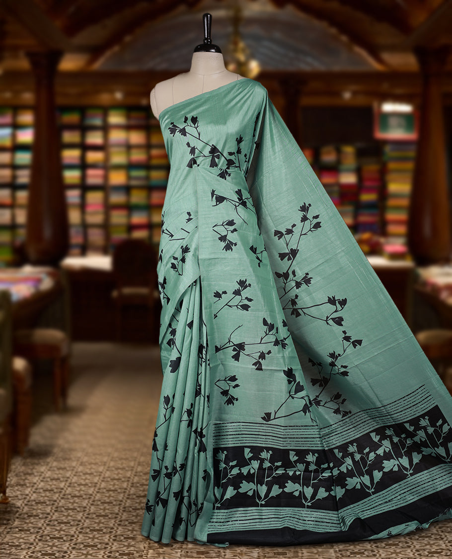 Pastel Green colour Semi tussar silk saree adorned with black floral prints on the body and an elegant pallu & Comes with a matching blouse piece for a classy look.