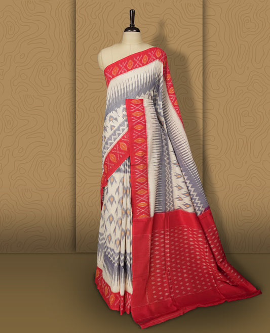 Off white colour Ikkat Pochampally saree adorned with blue & sandy brown geometric patterns, paired with a striking red border and pallu featuring traditional ikat motifs, a timeless blend of vibrance and tradition.