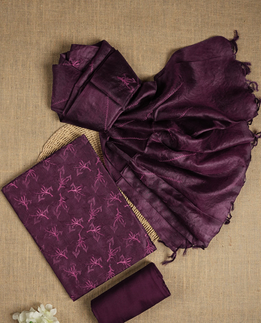 Dark grape colour tussar suit material featuring elegant floral thread embroidery on the body, paired with a soft dupatta adorned with matching embroidered motifs and tassel edges, along with a plain bottom piece.