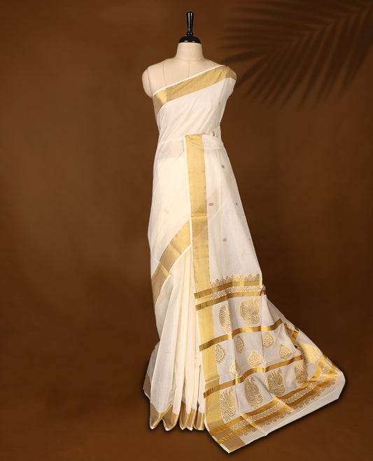 Traditional Kerala Kasavu saree in ivory with golden zari paisley motifs and a rich pallu, The graceful drape is perfect for festivals and weddings, Style with gold accessories for an elegant ethnic look.