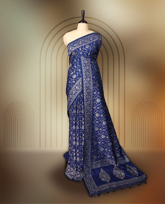 Blue Banaras soft silk saree with silver zari floral vines on the body, intricately woven border, and a grand pallu with bold paisley motifs, Comes with a matching blouse & perfect for elegant occasions.