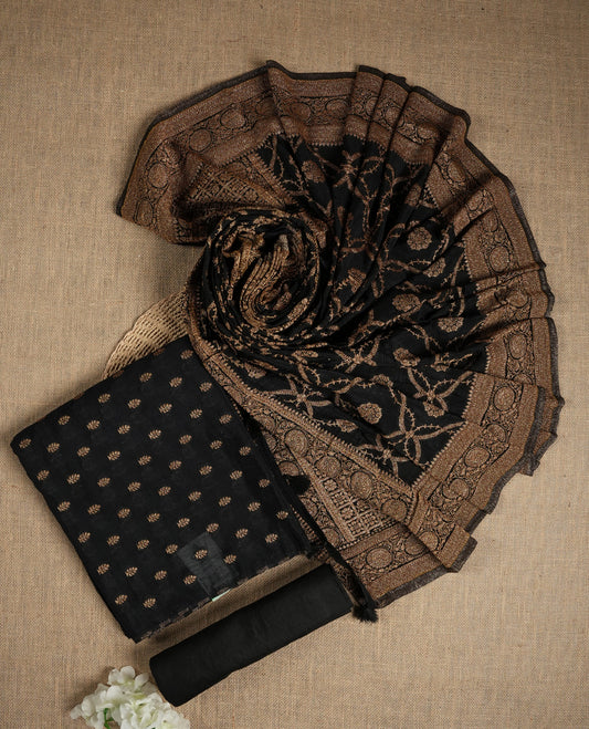 Black suit material adorned with intricate golden zari motifs weaving, exuding timeless elegance & Paired with a beautifully woven dupatta featuring floral and motifs and a matching plain bottom.