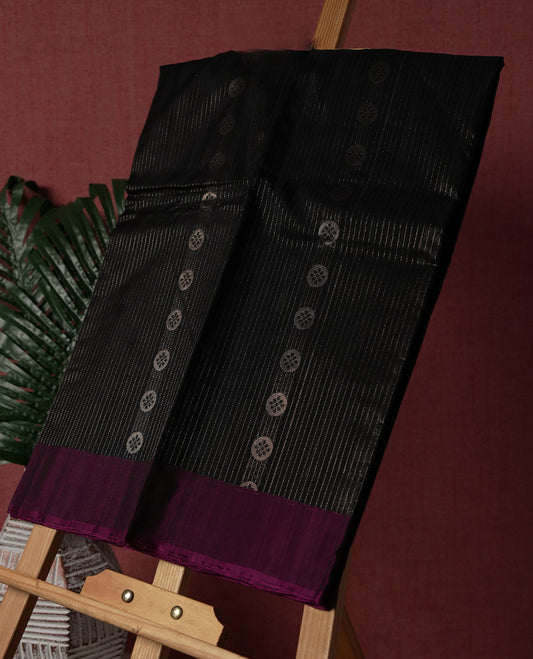 Black colour pure Handloom cotton saree featuring delicate rose gold zari stripes and motifs, paired with a rich purple border, perfect for graceful occasions & Comes with matching blouse.