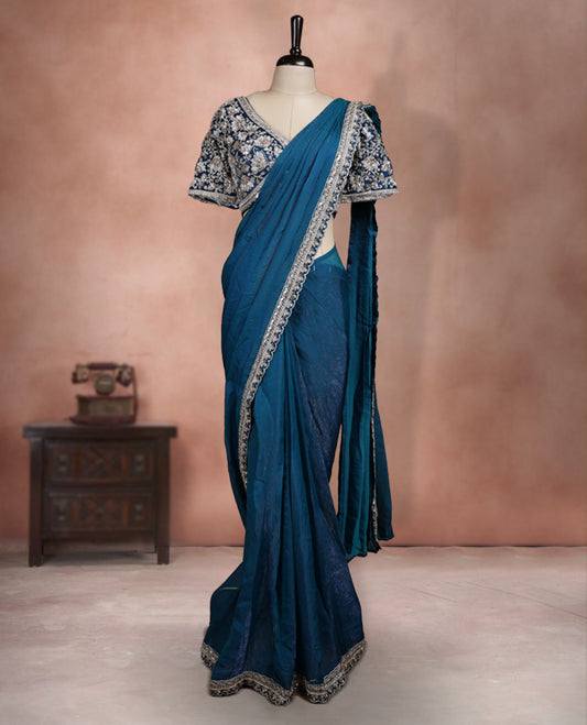 Elegant Teal Blue Colour ready to wear saree adorned with rich silver zari and bead embroidery along the border and pallu, paired with a heavily embellished matching blouse for a grand festive look.
