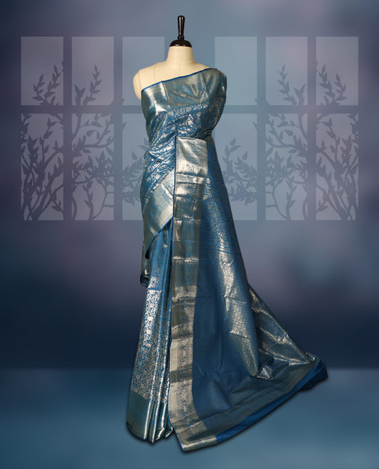Steel blue semi silk brocade saree featuring intricate silver brocade motifs across the body, enhanced by a gleaming silver woven border and pallu, Paired with a matching blouse for a refined traditional look.