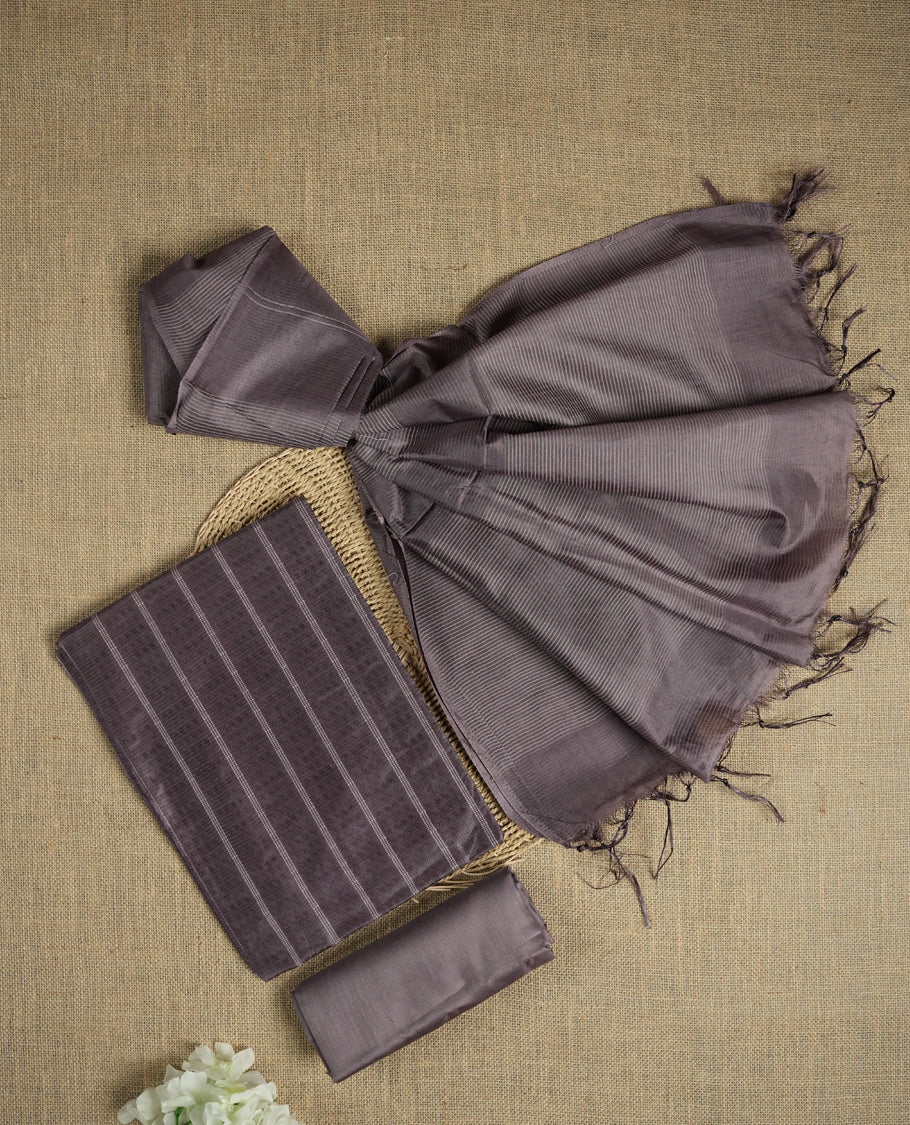 Dark pastel purple colour tussar suit material featuring a subtle self woven pattern and vertical lines on the body, paired with a lightweight matching dupatta with tassel edges and a plain bottom piece.