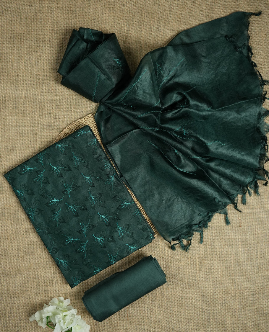 Deep jungle green colour tussar suit material featuring elegant floral thread embroidery on the body, paired with a soft dupatta adorned with matching embroidered motifs and tassel edges, along with a plain bottom piece.