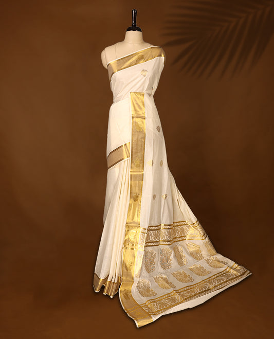 Elegant off white colour cotton Kerala saree embellished with golden buttas across the body and an ornate golden zari border and pallu featuring intricate motifs & A perfect traditional pick, paired with a matching blouse piece.