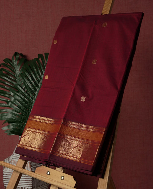 Maroon colour Pure Kanchi cotton saree adorned with subtle golden buttas all over, highlighted by a rich zari woven border with traditional motifs  & Includes a matching blouse piece for a complete look.