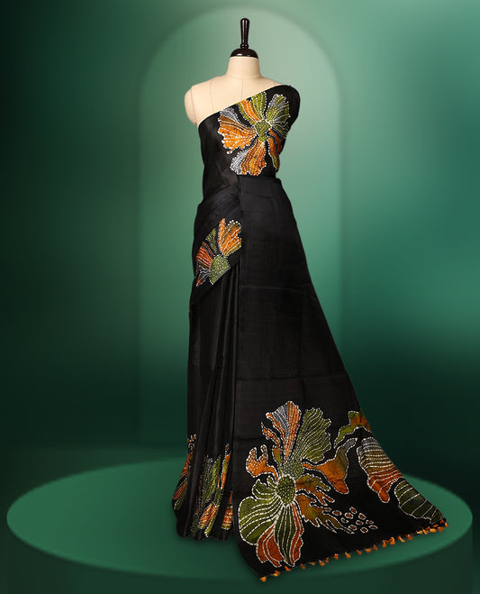Black colour semi tussar saree adorned with multi colour bold floral motifs across the body, designed without a border for a contemporary touch, and paired with a matching blouse