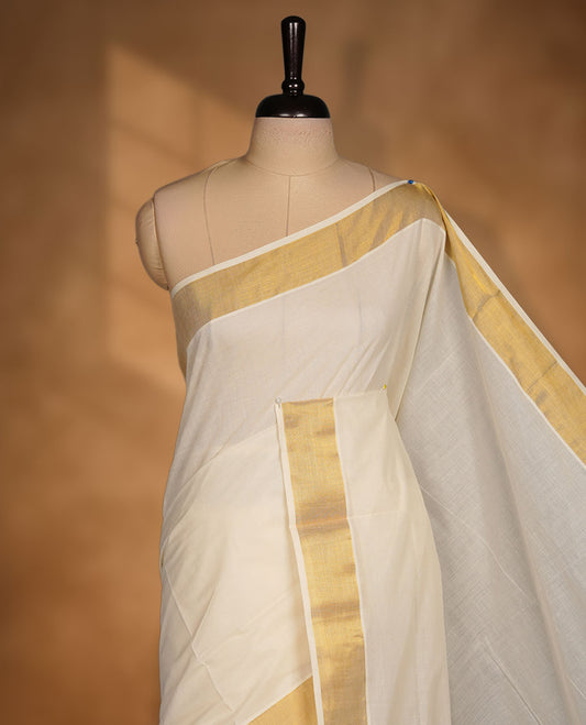 Off-white colour cotton Kerala saree crafted in a soft, sheer weave, finished with a classic gold kasavu border along the body and pallu, and paired with a matching blouse.
