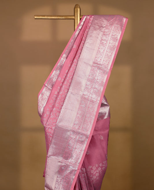 Light rose pink Colour traditional Kancheepuram silk saree adorned with antique zari small peacock motifs on the body, featuring a traditional border with light silver zari peacock and floral patterns, and paired with a matching blouse.
