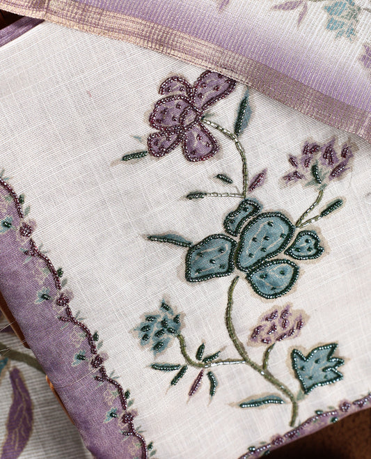 Beige & lavender colour churidhar material with floral print enhanced by sewn glass beads on the body, paired with plain lavender bottom & floral print dupatta.