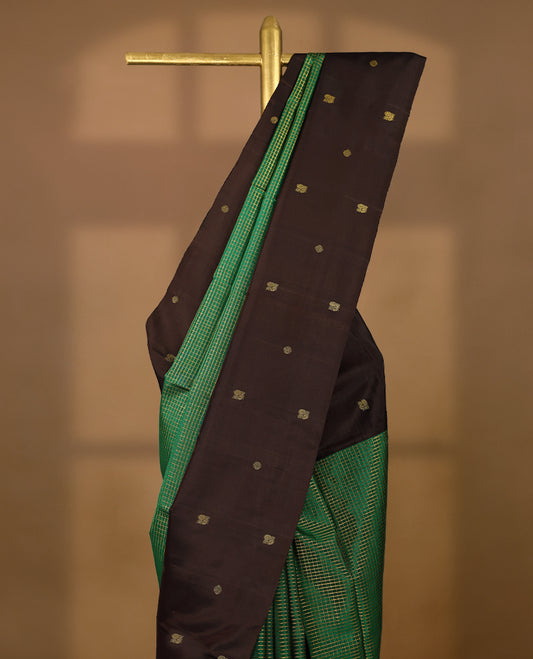 Green Colour pure traditional Kancheepuram silk saree featuring antique zari checks on the body, beautifully complemented by a dark chocolate simple border with delicate Chakkram and peacock motifs, and paired with a matching blouse.