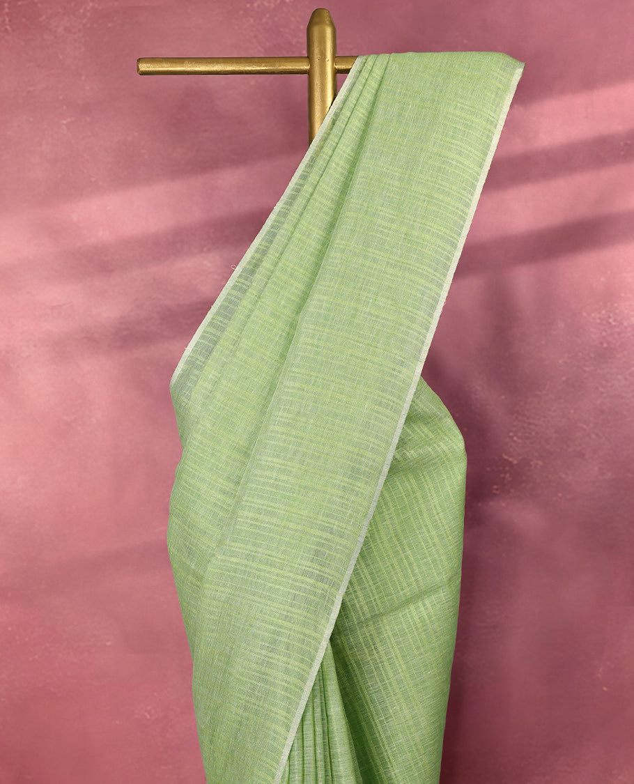 Pastel green colour pure linen saree adorned with delicate stripe patterns all over the body, highlighted with a simple white border and comes with a matching blouse