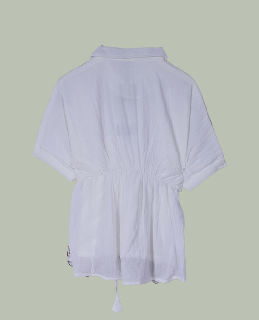 White short tunic top with collared neckline, short sleeves, multicolour paisley and floral embroidery on shoulders and hem, and a drawstring waist with long tasseled ties.