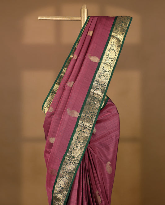 Solid mauve pink colour traditional Kancheepuram silk saree adorned with antique zari paisley motifs on the body, featuring a deep bottle green border with antique gold zari floral and vine patterns, and paired with a matching blouse.