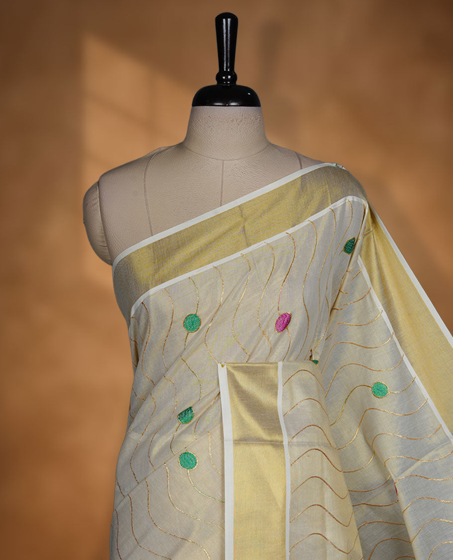 Off white colour cotton Kerala saree with wavy zari lines and colourful motifs, complemented by a classic golden zari border and matching blouse.