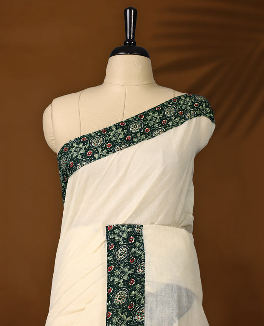 off white colour cotton Kerala saree adorned with a deep green border featuring intricate floral motifs in red and cream, paired with a matching printed blouse for a refined traditional look