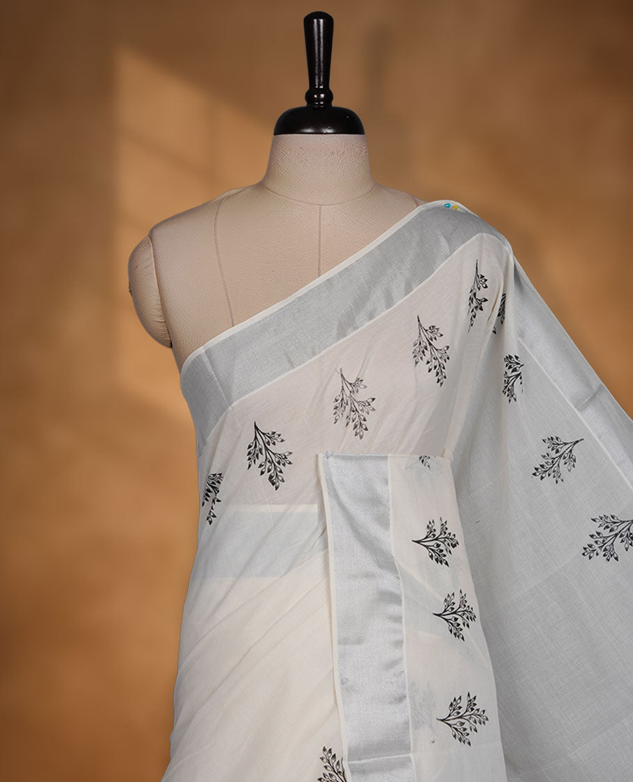 Off-white colour cotton Kerala saree featuring a subtle silver-toned border, adorned with delicate black leafy motifs across the body and pallu, and paired with a matching blouse.