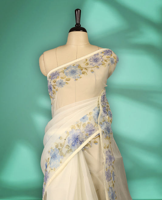 Ivory white colour organza saree adorned with blue floral print with thread detailing on the border and pallu, in a sheer finish that adds elegance, paired with a matching blouse for a graceful look.