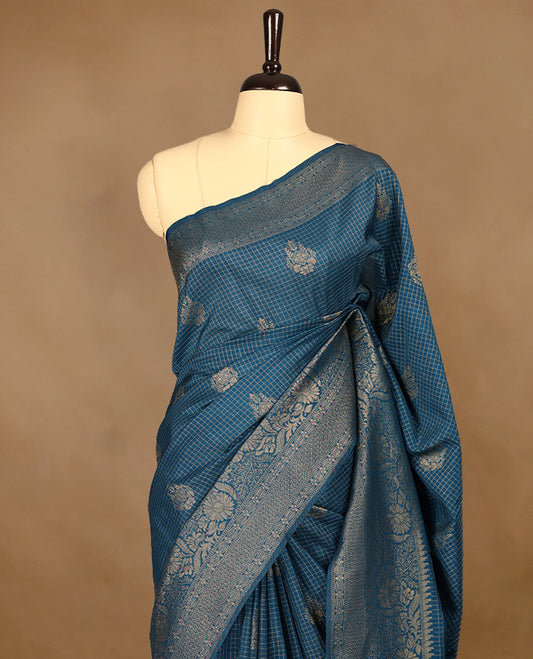 Blue coloured semi Banaras georgette saree featuring golden Zari checks with floral motifs on the body, complemented by a self coloured traditional border with floral kodi design and a matching blouse.