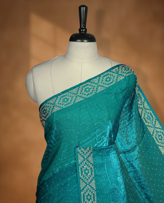 Teal colour chiffon designer saree, featuring delicate scattered stone detailing all over the body, highlighted with intricate stone work and a heavy geometric stone pattern along the border and pallu, paired with a matching embellished blouse.