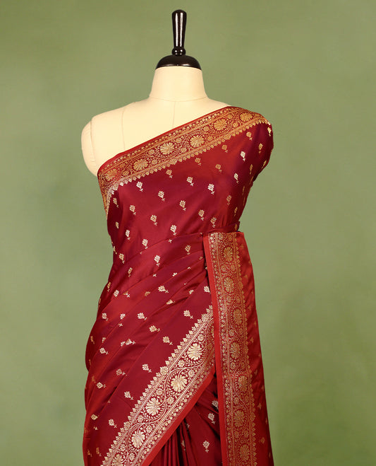 Deep red colour semi Banaras satin crepe saree featuring gold zari woven flower motifs across the body, complemented by an intricately designed traditional banarasi border and richly woven pallu, paired with a matching blouse piece.