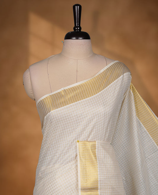Off-white colour cotton Kerala saree featuring a subtle golden checkered body, highlighted with a classic gold kasavu border accented by fine red lines, and finished with a matching cotton blouse.