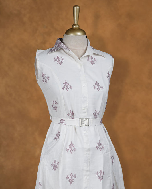 White sleeveless shirt dress with subtle mauve ethnic motifs, front button placket, matching waist belt with metal buckle, and ornate border print at hem.