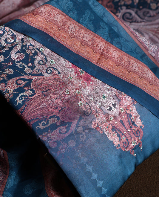 Dark peacock blue colour churidhar material with subtle paisley motifs, sequin highlights, and woven border design, paired with a plain matching bottom and a soft printed dupatta for a graceful ethnic look.