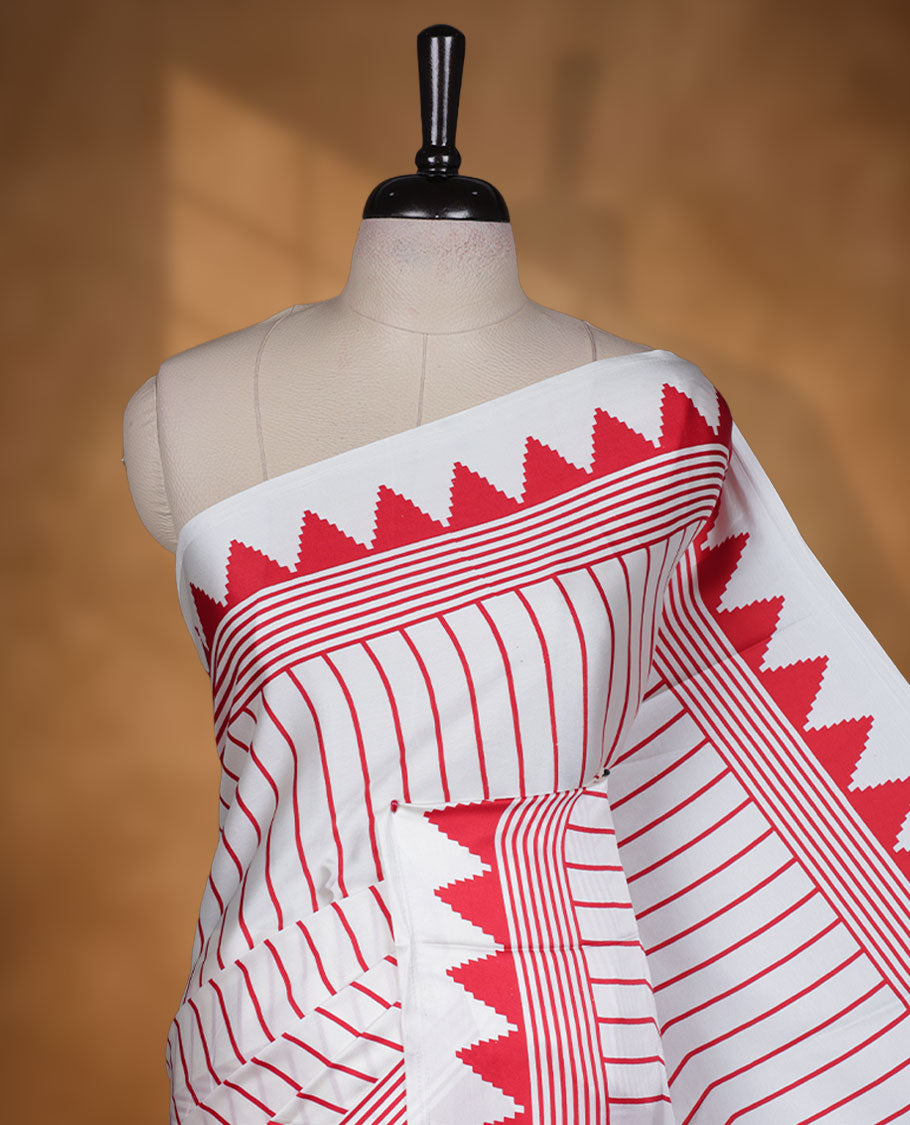 White colour semi modal saree highlighted with bold red triangle borders and fine striped detailing across the drape, featuring a striking oversized red circular motif on the pallu, paired with an all-over printed matching blouse.