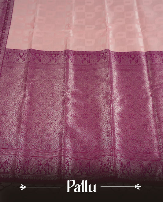 Pastel pink colour semi silk saree adorned with silver zari designs on the body, complemented by a contrasting purple border and pallu, and paired with a matching blouse piece.
