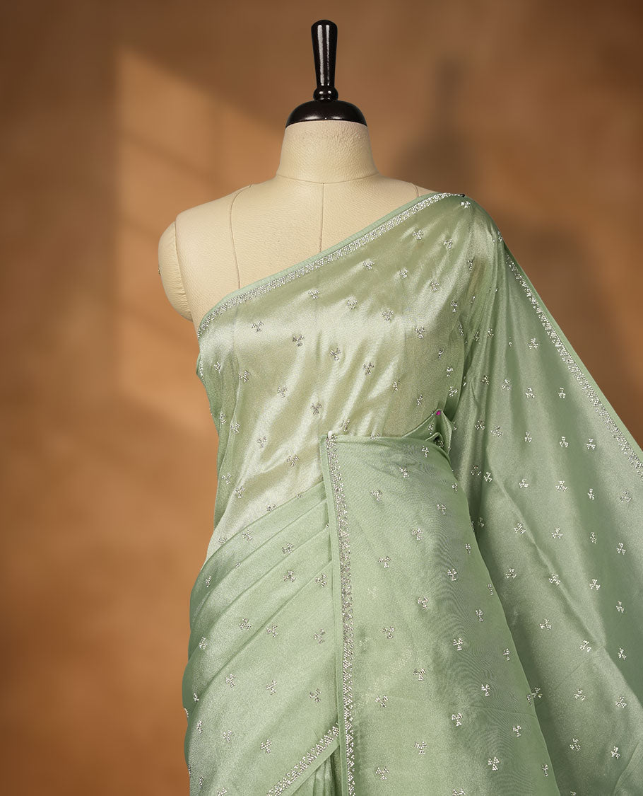Pastel Green Colour net shimmer fancy saree adorned with scattered white stone buttas all over the body, paired with a delicate stone worked border and matching blouse featuring floral vine stone embroidery.