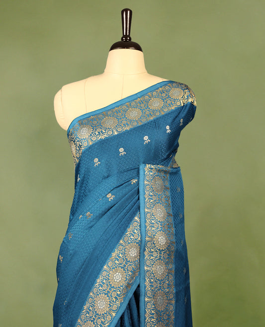 Blue colour pure Banaras crepe saree showcases elegant silver zari Flower Motifs all over the body, a traditional Banarasi gold zari border, a rich intricately woven pallu, and comes with a matching blouse.