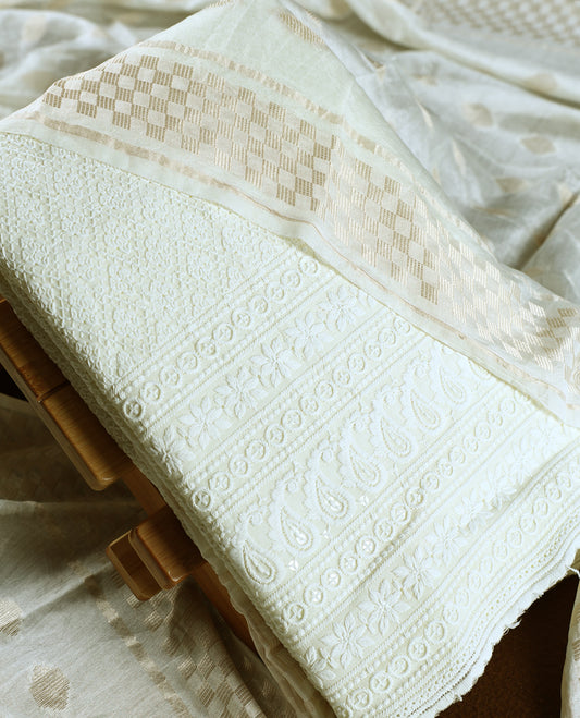 Off white colour churidhar material featuring delicate thread embroidery with paisley and floral motifs, paired with a plain bottom &  Comes with a soft dupatta woven with subtle golden zari patterns.